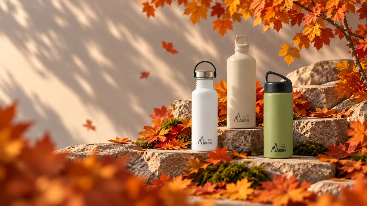 Tres botellas reutilizables LAKEN en tonos blanco, beige y verde oliva, rodeadas de hojas otoñales sobre piedras naturales. Selección de colores de otoño.