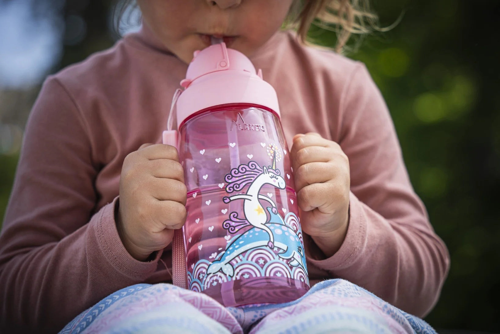 Niña sujetando una botella infantil LAKEN mientras bebe del tapón OBY